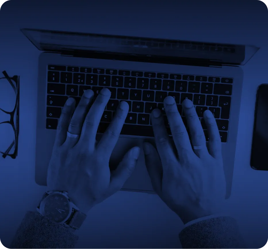 In der Vogelperspektive sieht man zwei Hände auf der Tastatur eines Laptops liegen. Links trägt die Personen einen Ring als auch eine Armbanduhr. Links vom Laptop liegt außerdem eine Brille. Das gesamte Bild ist in Blau und Schwarz gehalten